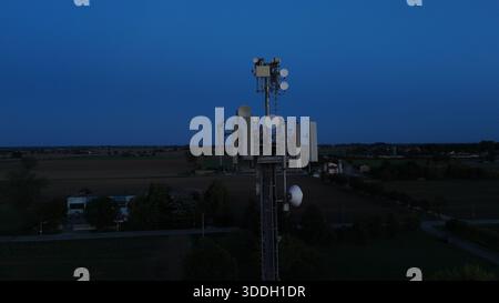 Mobilfunkturm steht vor dem dunkelblauen Himmel, ausgestattet mit verschiedenen Antennen für drahtlose Kommunikation und Mobilfunkdienste im gesamten Po Val Stockfoto