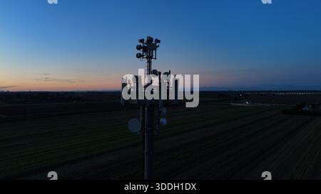 Mobilfunkturm steht vor dem dunkelblauen Himmel, ausgestattet mit verschiedenen Antennen für drahtlose Kommunikation und Mobilfunkdienste im gesamten Po Val Stockfoto