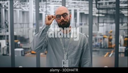 Bärtiger Ingenieur Mit Brille, Direkt Mit Professionellem Verhalten. Der Mann steht im High-Tech-Umfeld moderner Fertigungsstätten. Technisches Fachwissen und Innovation in der Industrie 4,0. Stockfoto