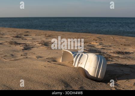 Entsorgte weiße Plastikkanne, halb begraben in Sandy Beach Shoreline Stockfoto