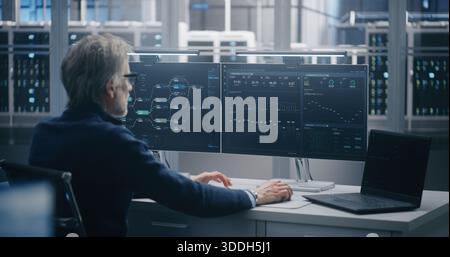 Leitender Techniker überwacht den Datenfluss auf zwei Bildschirmen und Laptops. IT-Spezialist, der an Monitoren arbeitet, die komplexe Netzwerkdiagramme und Analysen im Rechenzentrum anzeigen. Netzwerksicherheit und -Überwachung. Stockfoto
