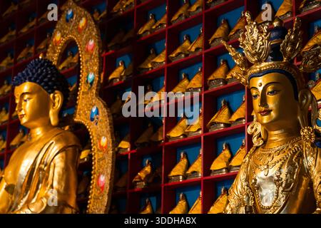 Goldene Buddha-Statuen im mongolischen Tempel mit bunten Miniaturhüten auf roten Wandregalen Stockfoto