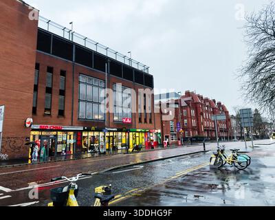 Manchester, Großbritannien - 06. Dezember 2025: Regnerischer Tag auf einer Manchester Street mit Ziegelfassaden, Fahrrädern und Ladenfronten. Stockfoto