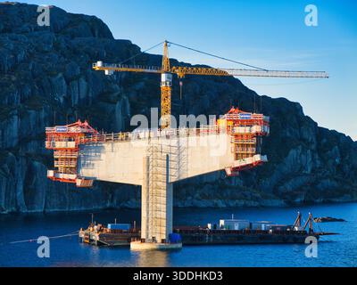 Küste, Norwegen - 25. November 2025: Brückenpier im Bau mit Turmkran und Gerüsten über einem Fjord an der norwegischen Küste, beleuchtet durch klares Winterlicht. Stockfoto