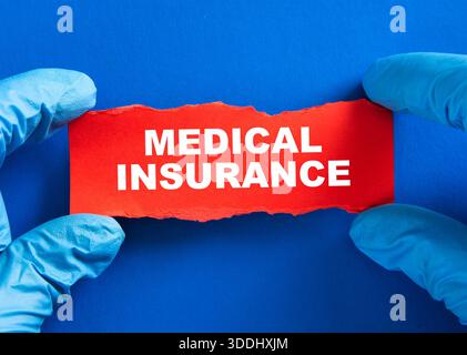 Hände in blauen medizinischen Handschuhen, die rotes Papier mit Krankenversicherungstext halten Stockfoto