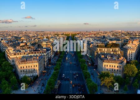 Weite Aussicht auf die Avenue des Champs Elysees, die sich durch das Zentrum von Paris erstreckt, gesäumt von eleganten Haussmann-Gebäuden und grünen Bäumen in warmer Abendsonne unter einem klaren blauen Himmel. Stockfoto