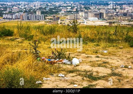 Müll über den Hügel mit Bischkek Stadt im Hintergrund. Plastikflaschen und Müllbeutel stehen im Kontrast zur umgebenden Vegetation und betonen die Vernachlässigung der Umwelt bei Tageslicht. Stockfoto