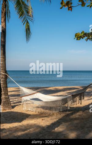 Friedliche weiße Hängematte an einem sonnenverwöhnten tropischen Strand mit Palmen und Meerblick Stockfoto