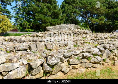 Der antike Trockenturm erhebt sich auf geschichteten Terrassen unter hohen grünen Bäumen am Locmariaquer. Das Sonnenlicht hebt die verwitterten Felsen und natürlichen Strukturen hervor und erweckt ein Gefühl historischer Geheimnisse. Stockfoto