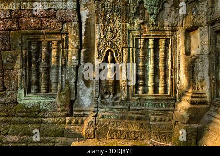 Das komplizierte Basrelief einer apsara-Tänzerin und die detaillierten Steinfenster-Säulen werden durch warmes Sonnenlicht auf der verwitterten Wand des Ta Nei Tempels in Angkor, Kambodscha, beleuchtet. Das alte Khmer-Mauerwerk zeigt feine Schnitzereien, strukturierte Oberflächen und subtiles Moos in einer ruhigen Waldruine. Stockfoto