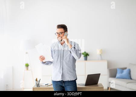 Home Office-Konzept. Selbstbewusster Millennial-Unternehmer, der am Handy spricht und Finanzberichte diskutiert Stockfoto
