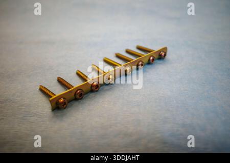 Hochauflösende Nahaufnahme einer goldfarbenen orthopädischen Knochenplatte mit mehreren nacheinander montierten chirurgischen Schrauben, die auf einer sterilen blu-ray-Platte platziert sind Stockfoto