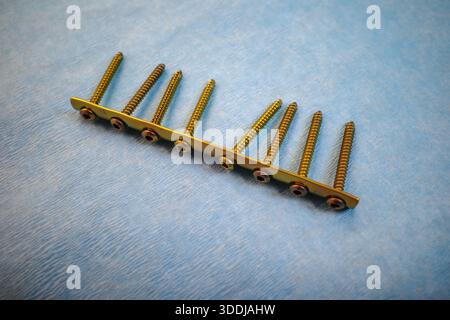 Hochauflösende Nahaufnahme einer goldfarbenen orthopädischen Knochenplatte mit mehreren nacheinander montierten chirurgischen Schrauben, die auf einer sterilen blu-ray-Platte platziert sind Stockfoto
