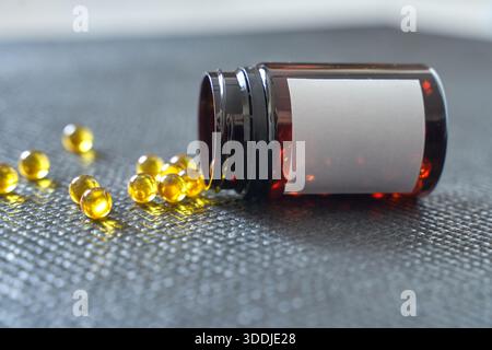 Braunglasflasche mit verschütteten gelben Kapseln auf dunkler Oberfläche für Gesundheits- und Wellnesskonzept. Stockfoto