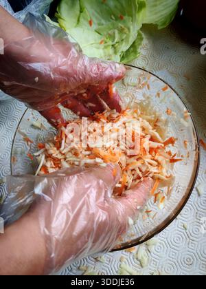 Man trägt transparente Handschuhe, während man Kohl und Karotten in einer Glasschale mischt. Stockfoto