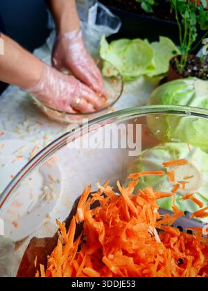 Man trägt transparente Handschuhe, während man Kohl und Karotten in einer Glasschale mischt. Stockfoto
