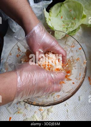 Man trägt transparente Handschuhe, während man Kohl und Karotten in einer Glasschale mischt. Stockfoto