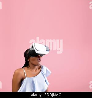 Cyberspace. Schockierte afroamerikanische Frau mit VR-Helm, die virtuelle Realität auf rosa Hintergrund erlebt Stockfoto