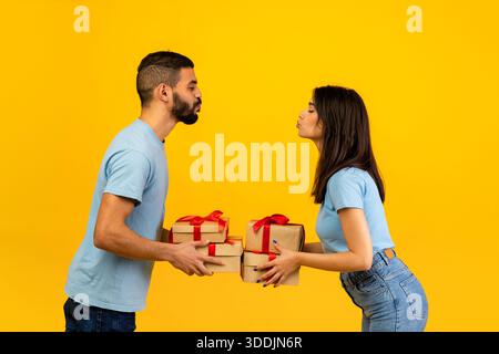 Romantisches arabisches Paar, das Geschenke und Küsse auf gelbem Hintergrund für besondere Anlässe teilt Stockfoto