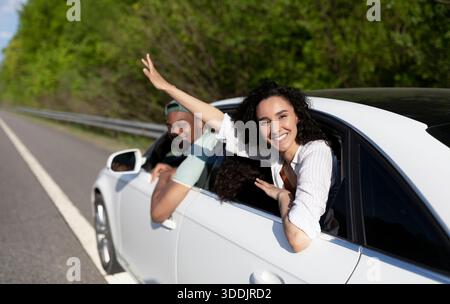Die besten Freunde aus verschiedenen Rassen, die zusammen mit dem Auto reisen, durch Fenster schauen und im Sommer eine lustige Reise machen Stockfoto