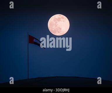 Vollmond in einem klaren Nachthimmel über der Flagge der Vereinigten Arabischen Emirate auf einem Gipfel der Mall of the Emirates. Stockfoto