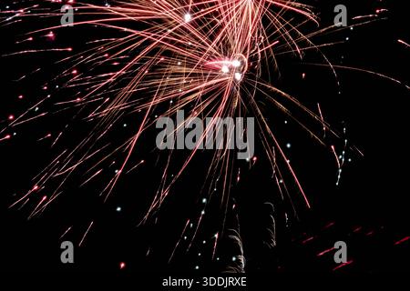Abstraktes Langzeitfoto eines Feuerwerks, das dichte, bunte Lichtspuren mit leuchtenden Lichtern vor einem tiefschwarzen Nachthimmel schafft. Dynami Stockfoto