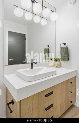 Badezimmer mit weißem Waschbecken und grünem Handtuch an der Wand. Das Waschbecken befindet sich vor einem Spiegel und eine Leuchte darüber Stockfoto