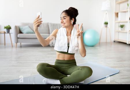 Fröhliche indische Frau nimmt Selfie auf Pause von zu Hause Workout, in voller Länge Stockfoto