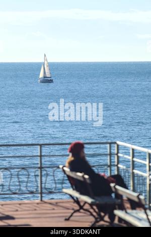 Segelboot auf dem Meer, von einem Balkon aus gesehen, mit einer unfokussierten Frau, die auf einer Bank sitzt Stockfoto