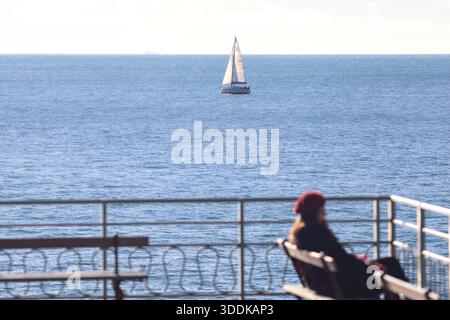 Segelboot auf dem Meer, von einem Balkon aus gesehen, mit einer unfokussierten Frau, die auf einer Bank sitzt Stockfoto