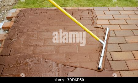 Aufbringen der Fugenmischung auf der neuen Pflastersteinterrasse Stockfoto
