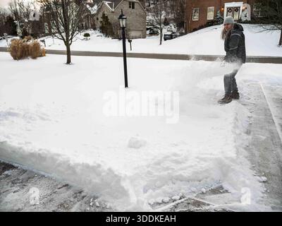 Ein Hausbesitzer wirft eine Schaufel frischen weißen Schnees in die Luft, während er seine Vorstadteinfahrt nach einem Schneesturm räumt. Stockfoto