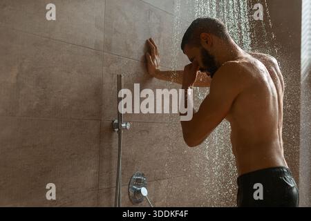 Junger Mann genießt eine erfrischende Dusche in einem modernen Badezimmer zu Hause für die tägliche Pflege Stockfoto