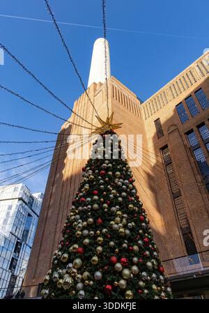 Hoher, geschmückter Weihnachtsbaum mit festlichen Lichtern vor dem Battersea-Kraftwerksgebäude mit weißem Kamin an einem klaren blauen Himmel Stockfoto