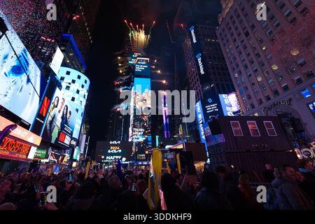 Eine nächtliche Menschenmenge am Times Square feiert Silvester mit Feuerwerk, Konfetti und beleuchteten Plakaten, die die festliche Atmosphäre einfangen. Stockfoto