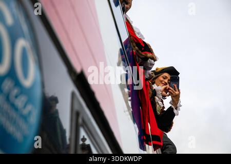 Eine Darstellerin nutzt ihr Handy, um während der Neujahrsparade Fotos von einem offenen Bus zu machen. Die Londoner Neujahrsparade, die seit 1987 jährlich am 1. Januar stattfindet, zeigt mehr als 8.000 Teilnehmer, darunter internationale Bands, Cheerleader, große Inflatables und Floats, von Piccadilly nach Westminster. Die Parade zieht bis zu einer Million Zuschauer an, die die Veranstaltung kostenlos auf einer Route beobachten, die an bedeutenden Sehenswürdigkeiten wie dem Piccadilly Circus und dem Trafalgar Square vorbeiführt und eine Feier der globalen Musik und Kultur bietet. Stockfoto