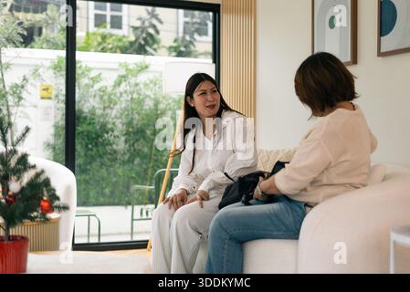 Frauen, die auf dem Sofa sitzen und sich unterhalten, teilen ihre Tasche im modernen Wohnzimmer Stockfoto