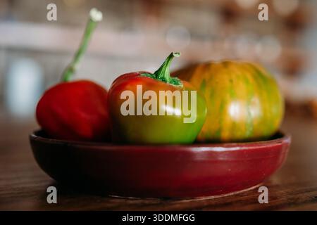 Bunte Paprika und gestreifte Tomaten in roter Schüssel Stockfoto