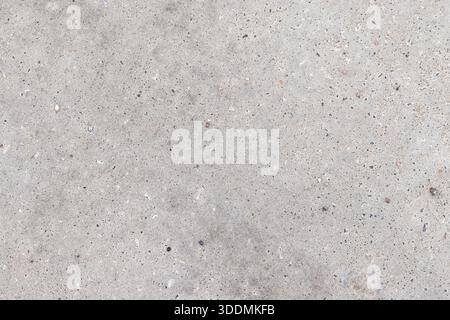 Nahaufnahme eines grauen Betonpflasters mit verstreuten Sandkörnern und winzigen Kieselsteinen. Idealer Hintergrund für Städte, Industrie oder Bauwesen Stockfoto