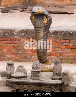 Vor einer Ziegelmauer steht eine detaillierte Steinkobra-Skulptur, die Stärke und traditionelle künstlerische Handwerkskunst symbolisiert. Stockfoto