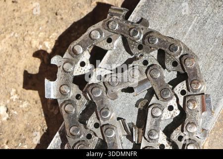Nahaufnahme einer schmutzigen schweren Metallsägekette auf Holztisch mit gefährlichem Aussehen und glänzender Stahlstruktur, die industrielle Festigkeit für harte Arbeiten zeigt Stockfoto