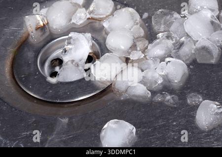 Schmelzende Eiswürfel tropfen in einen Waschbecken-Stopfen und lassen das silberne Metallbecken ab Stockfoto