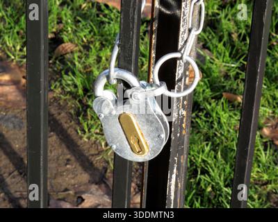 Nahaufnahme eines robusten neuen Vorhängeschlosses aus Stahl und einer Kette, die sicher an einem Metallzaun-Tor verriegelt ist und den Schutz von Sachwerten, eingeschränkten Zugang und Safe darstellt Stockfoto