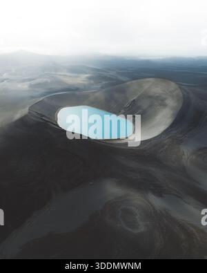 Aus der Vogelperspektive auf einen auffallend blauen Gletschersee, eingebettet in eine dunkle, vulkanische, außerirdische Landschaft, Highlands, Island. Stockfoto
