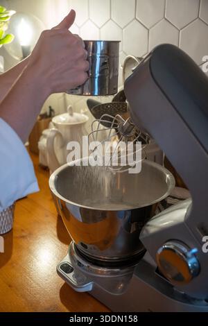 Sieben Sie das Mehl mit den Händen in den Mixer, während Sie den Apfel charlotte-Teig auf einer hölzernen Küchentheke zubereiten, um den konzentrierten Moment des Backens zu Hause festzuhalten Stockfoto