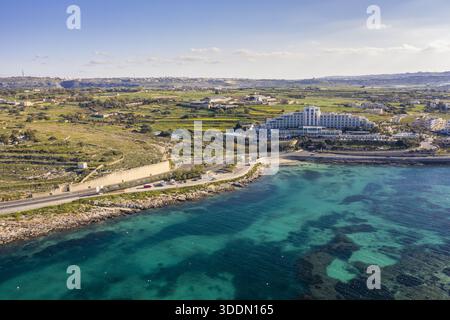 Blick aus der Vogelperspektive auf türkisfarbenes Wasser, das die felsige Küste in der Nähe eines weitläufigen Hotelkomplexes trifft, Bugibba, St. Paul's Bay, Malta. Stockfoto