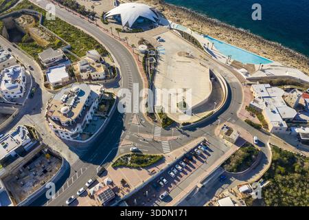 Blick aus der Vogelperspektive auf den pulsierenden Kreisverkehr in der Nähe der schimmernden Küste und die unverwechselbare kuppelförmige Struktur, Bugibba, St. Paul's Bay, Malta. Stockfoto