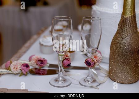 Elegante Sektflöten zur Hochzeit mit Blumen und Glitzerflaschen im Hintergrund Stockfoto