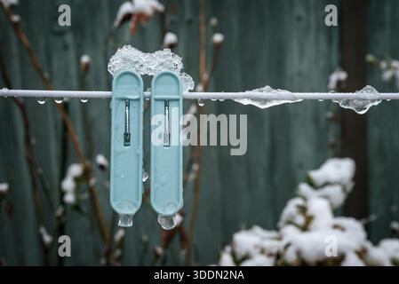 Nahaufnahme aus Stoffaufhängeclips und Seil mit Eis und Schnee, die winterliche Texturen und saisonale Veränderungen hervorheben -A Stockfoto