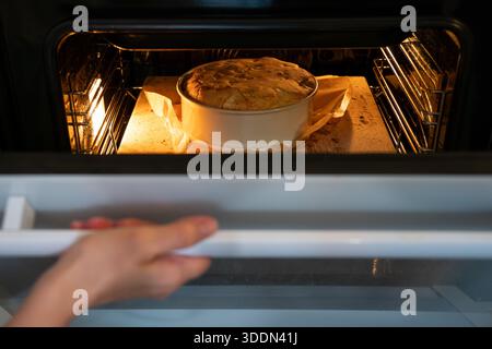 Apple charlotte Kuchen backen in einem Ofen in einer runden Pfanne, beleuchtet von warmem Ofenlicht, zeigt aufsteigenden Teig und eine gemütliche hausgemachte Backstimmung Stockfoto